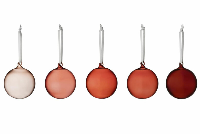 enfeites de bola de vidro em tons finos em tons de rosa e vermelho pendurados na frente de um fundo branco