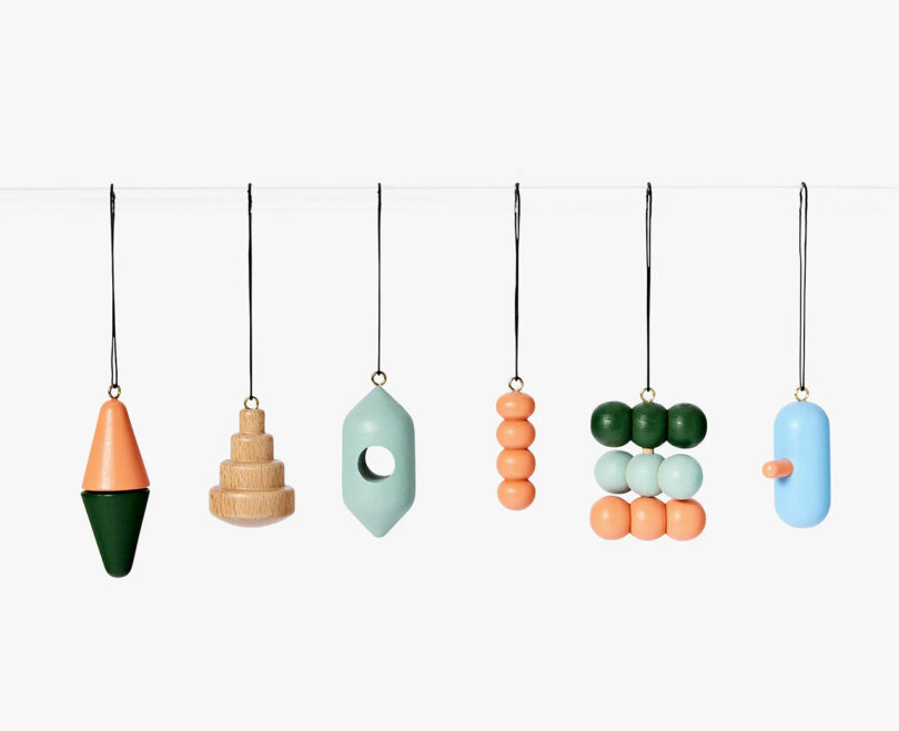 six painted wooden ornaments hanging on string side by side