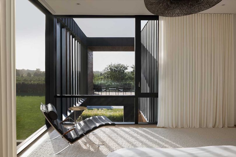 interior view of modern house in upper corner with glass windows on two sides with black lounge chair in front