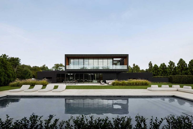 daytime exterior shot of modern two-story black house with swimming pool in front