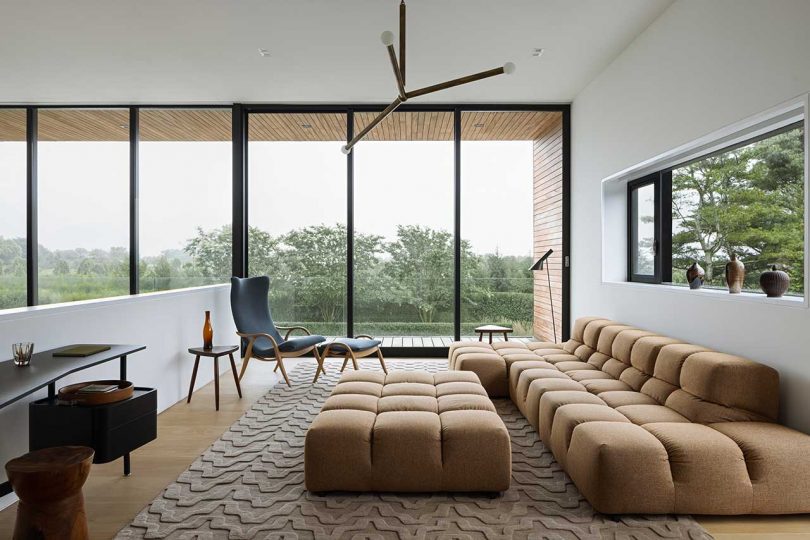 upstairs sitting area of modern hoe with camel colored modular sofa and floor-to-ceiling windows with views