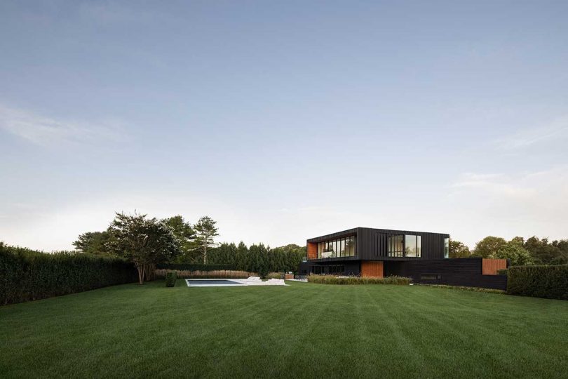 daytime exterior side shot of modern two-story black house with swimming pool