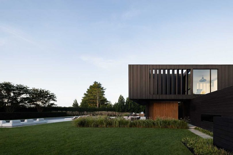 daytime exterior side shot of modern two-story black house with swimming pool