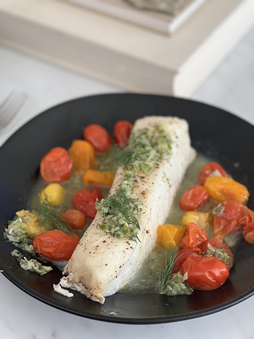 plated dish of fish and burst tomatoes on a black plate
