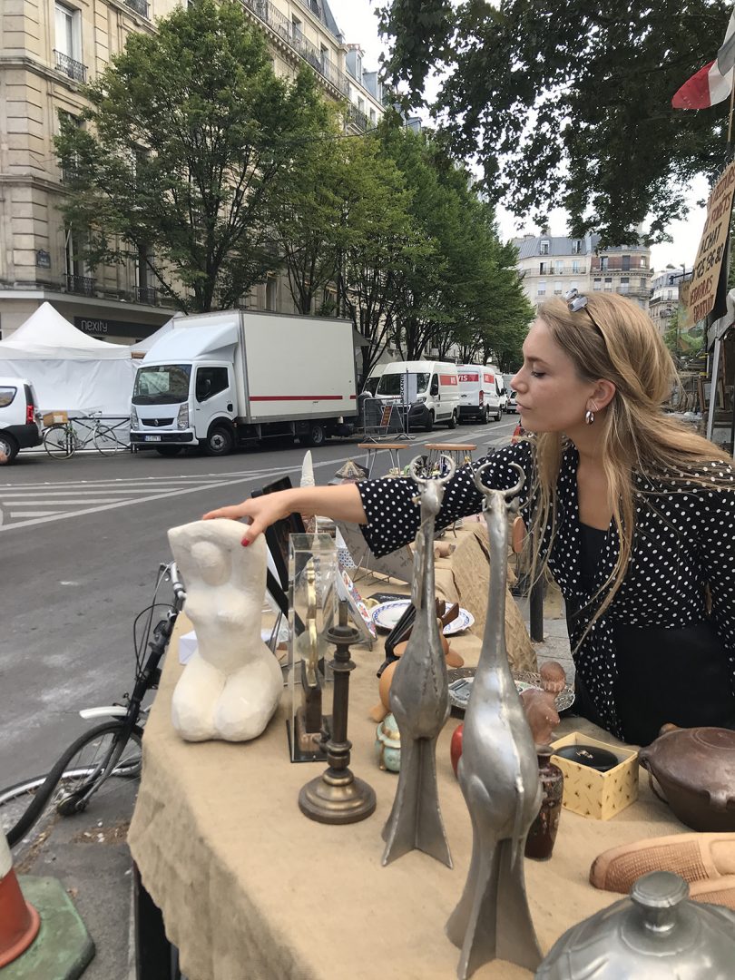 light-skinned blonde-haired woman reaching across a table at a flea market