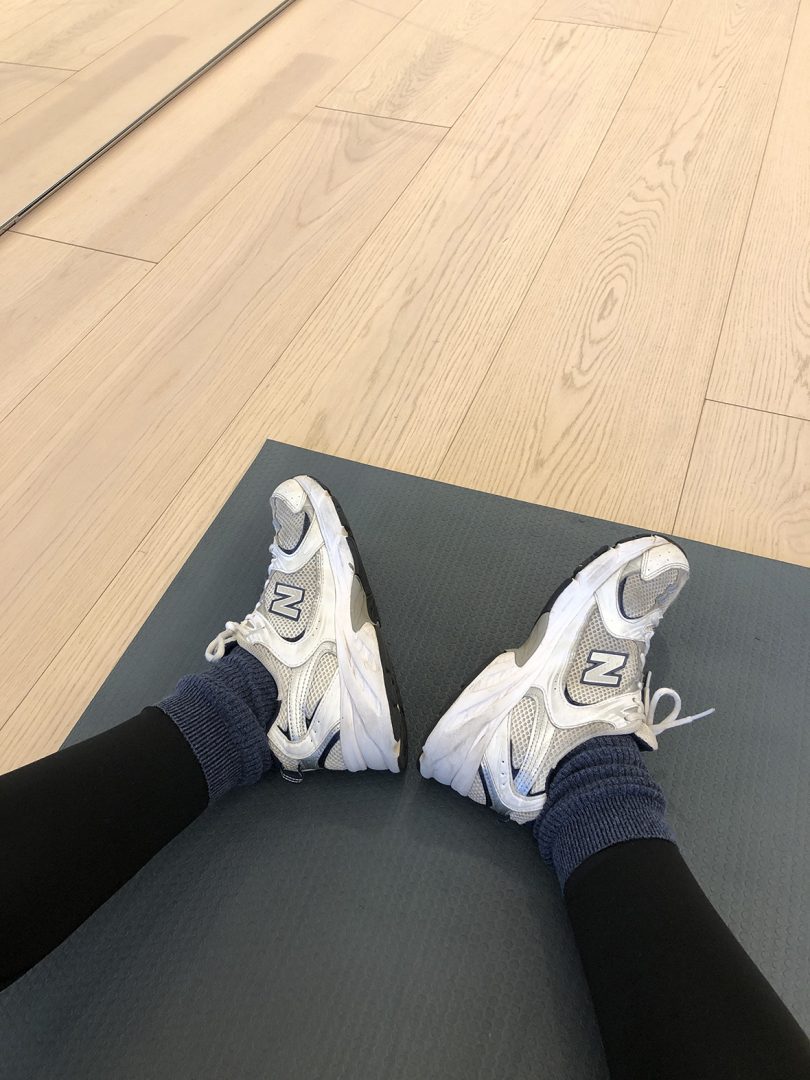 POV image looking down and legs wearing black leggings and white sneakers on a yoga mat