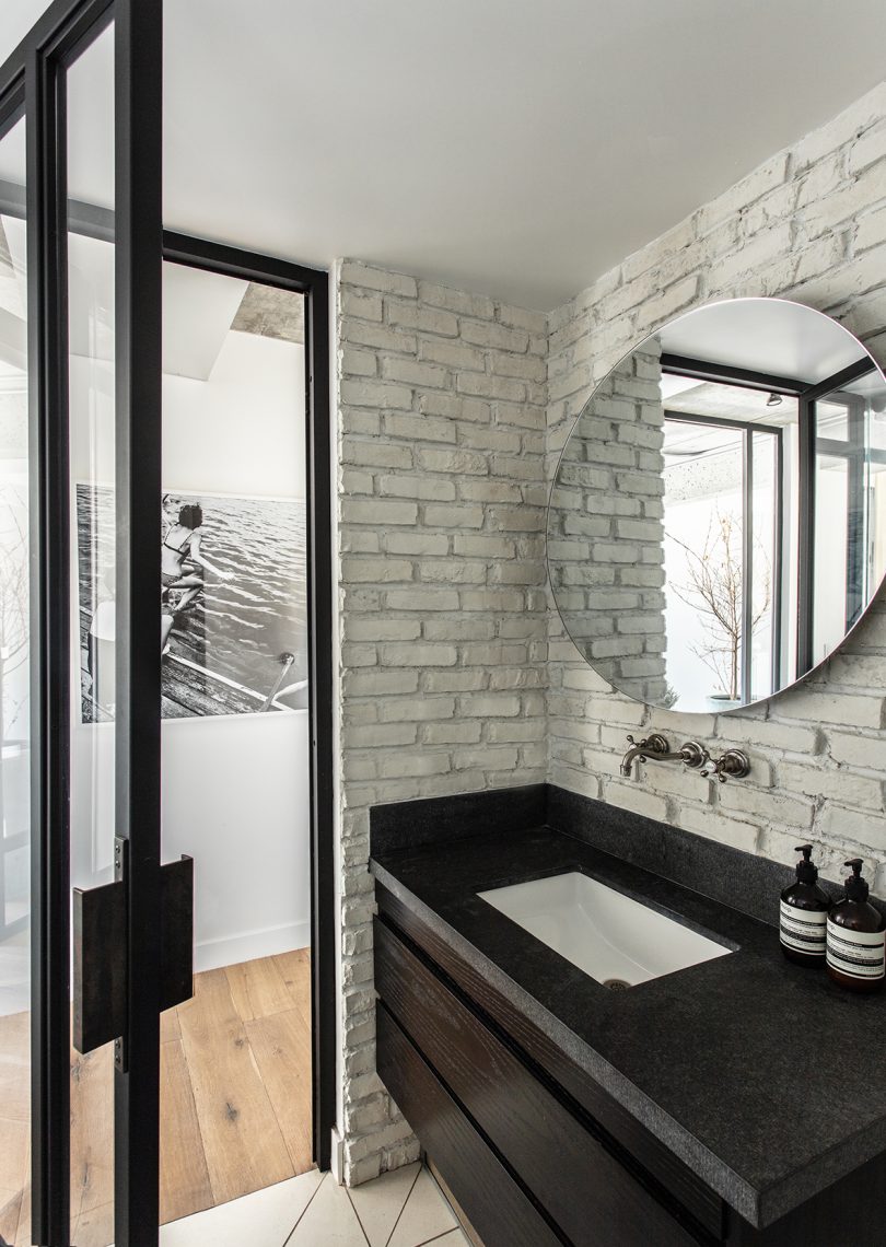 bathroom with dark counter, white sink, wall-mount fixtures, and round mirror