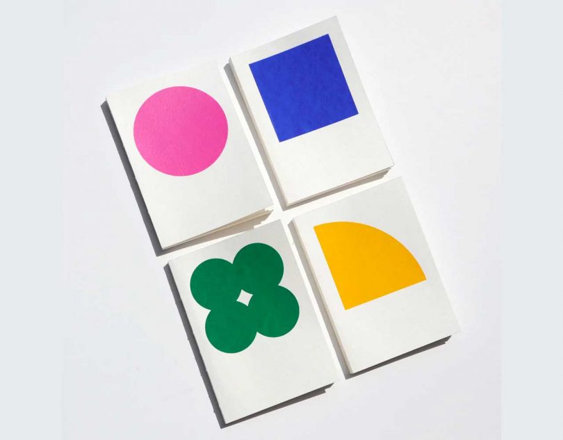 four white notebooks each with a colorful shape