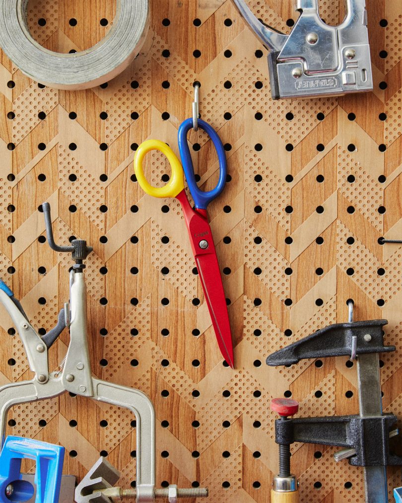 primary colored pair of scissors hanging on wood pegboard with other tools