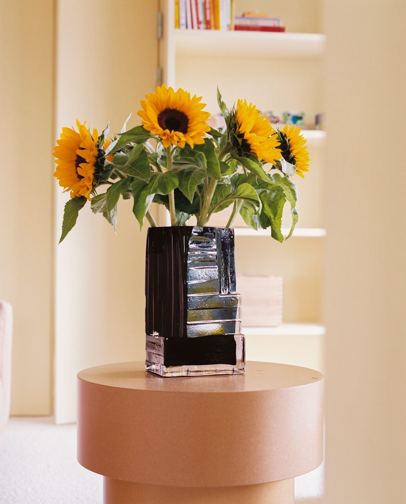 black glass vase with sunflowers flowers on a side table