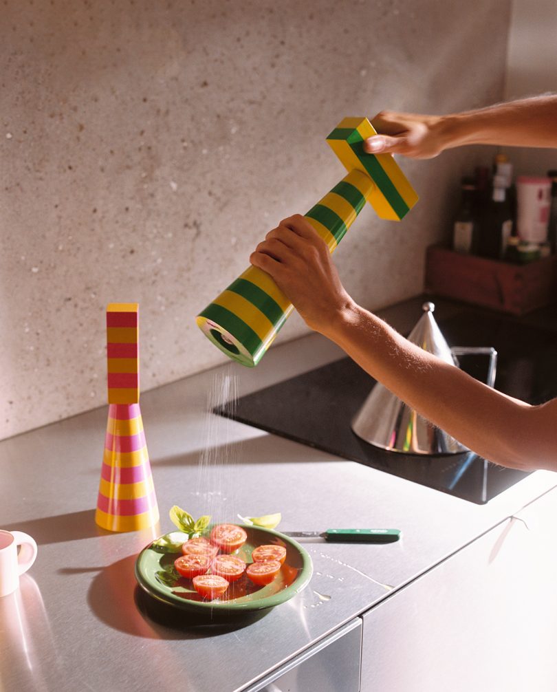 a person uses a colorful striped salt or pepper grinder to season a plate of tomatoes