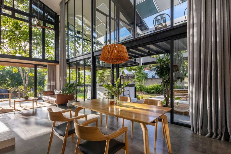 angled interior shot of modern house with double height ceiling looking out glass walls to green exterior