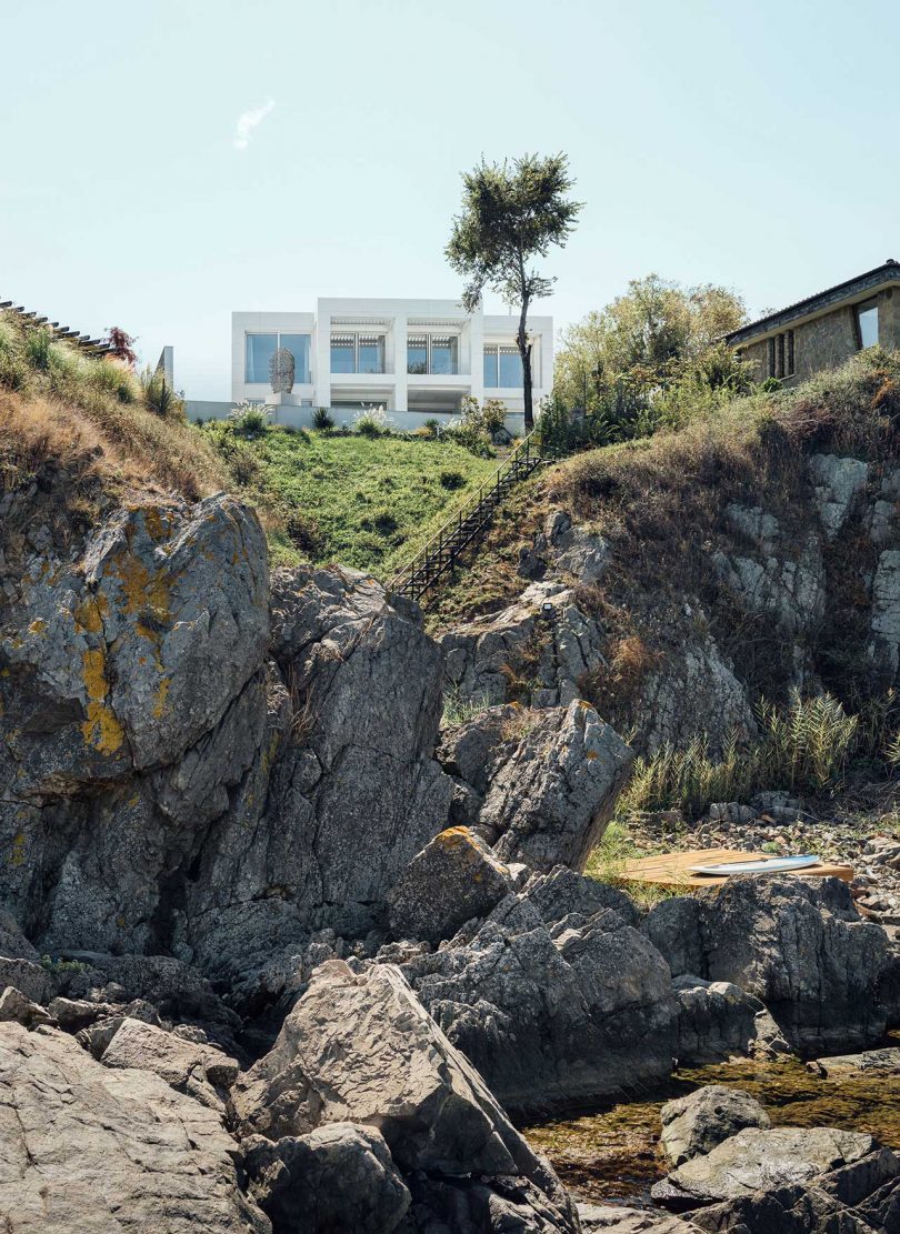 exterior view of minimalist, all-white modern house on top of rocky cliff 