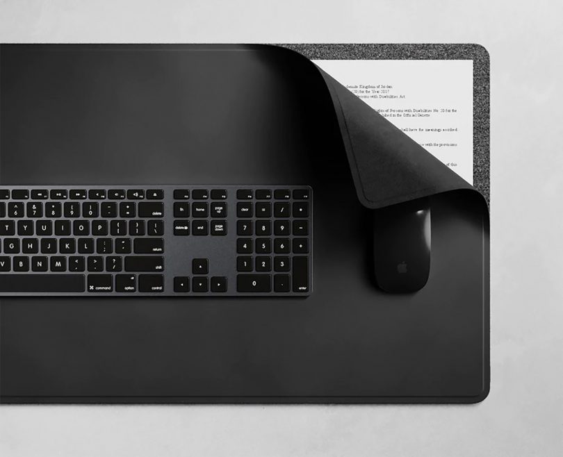 Black ALTI wireless charging desk mat with black keyboard and mouse, with upper right hand corner curled to reveal documents tucked inside.
