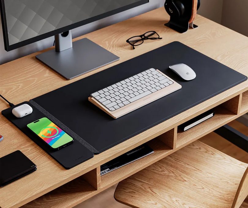Desk set up with black ALTI wireless charging desk mat with monitor setup and eyeglasses and headphones nearby.