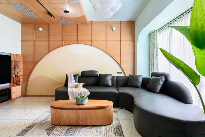 modern apartment interior with curved black leather sofa, cloud-like pendant, and abstract wall design