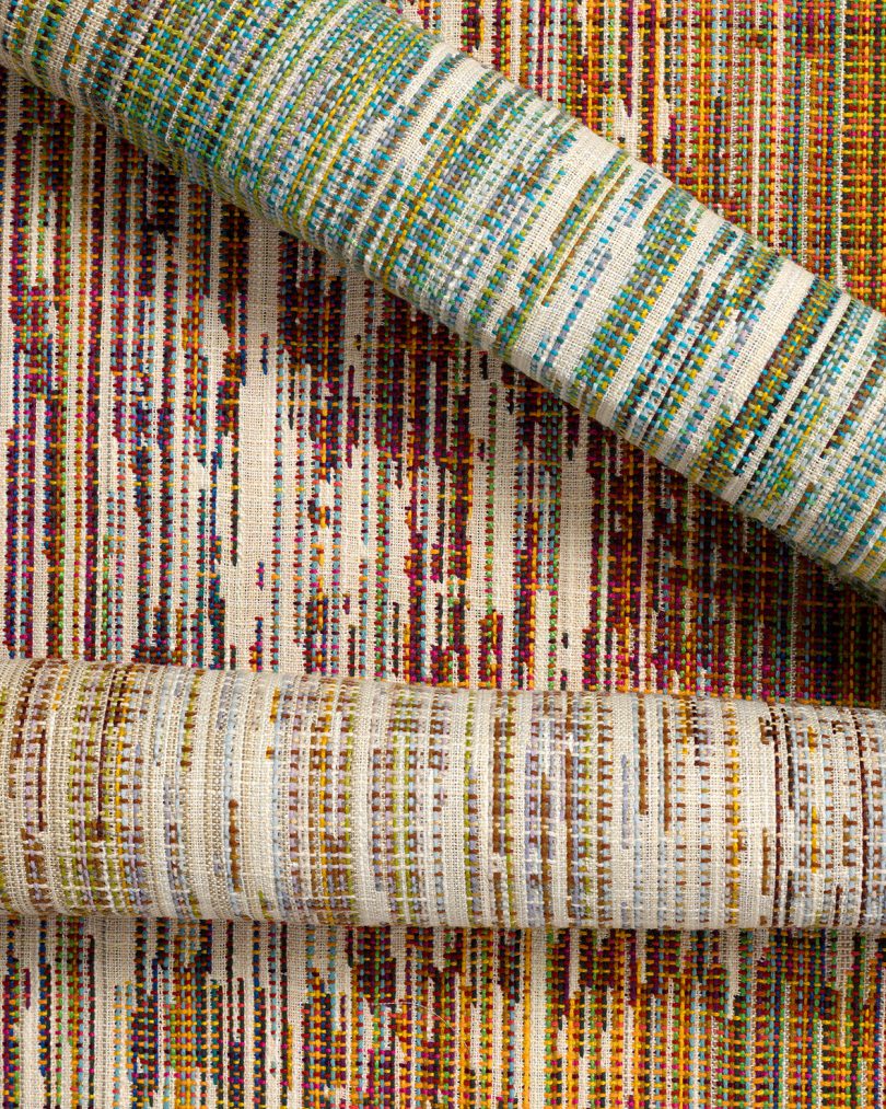 two rolls of wallcoverings laying on top upholstery patterned in warm hues and vertical strokes