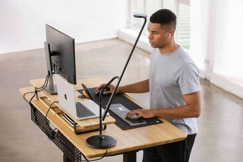 styled light wood and black office desk with brown-skinned man standing behind it working
