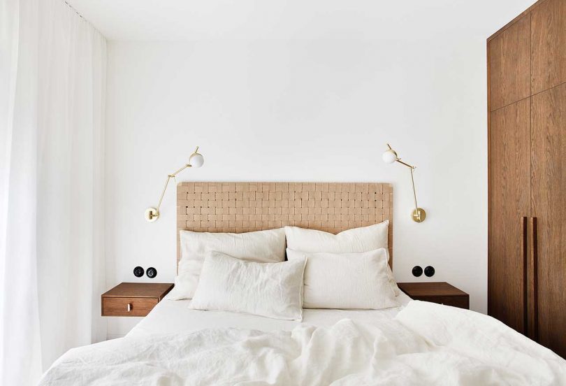 نمای تخت مینیمالیستی با تخت خواب سبک و ملافه سفید در اتاق خواب مدرن سفید