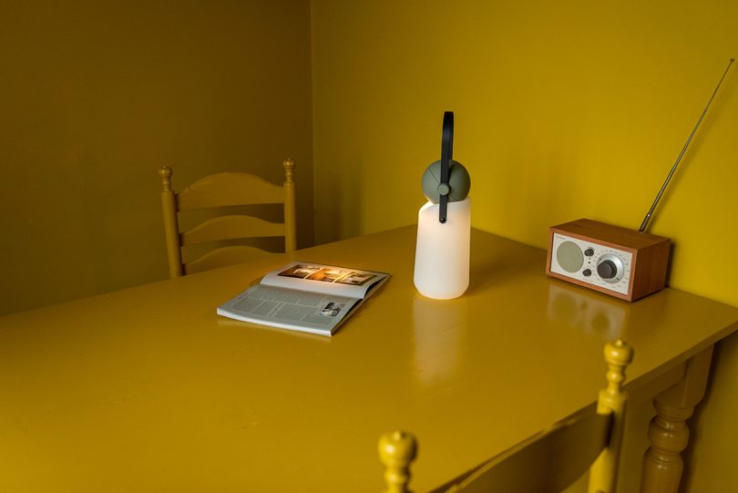 portable lamp with a white base, grey top, and black strap handle sitting on a bright yellow dining table