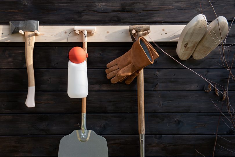 portable lamp with a white base, red top, and black strap handle hanging on a hook with outdoor tools