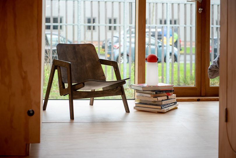 portable lamp with a white base, red top, and black strap handle sitting on a stack of books next to an armchair