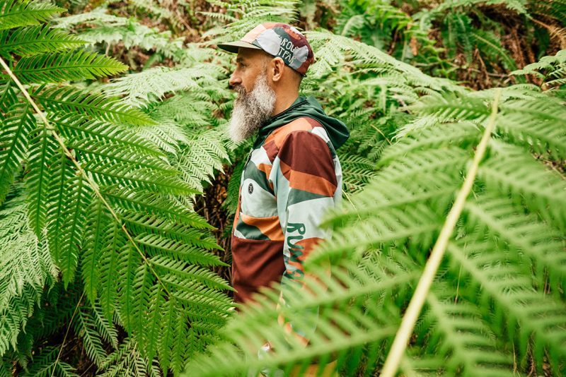 Artist Travis Weller standing sideways amongst ferns.