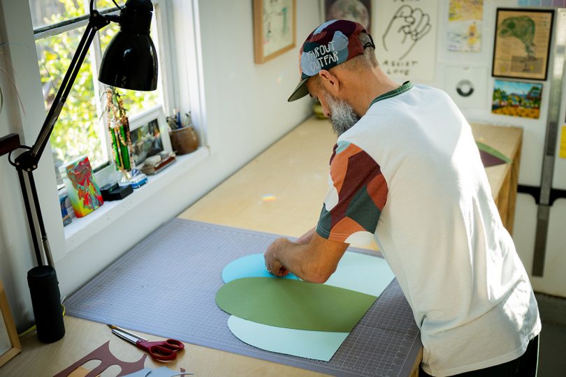 Artist Travis Weller from overhead shown cutting pieces of colored paper for composition..
