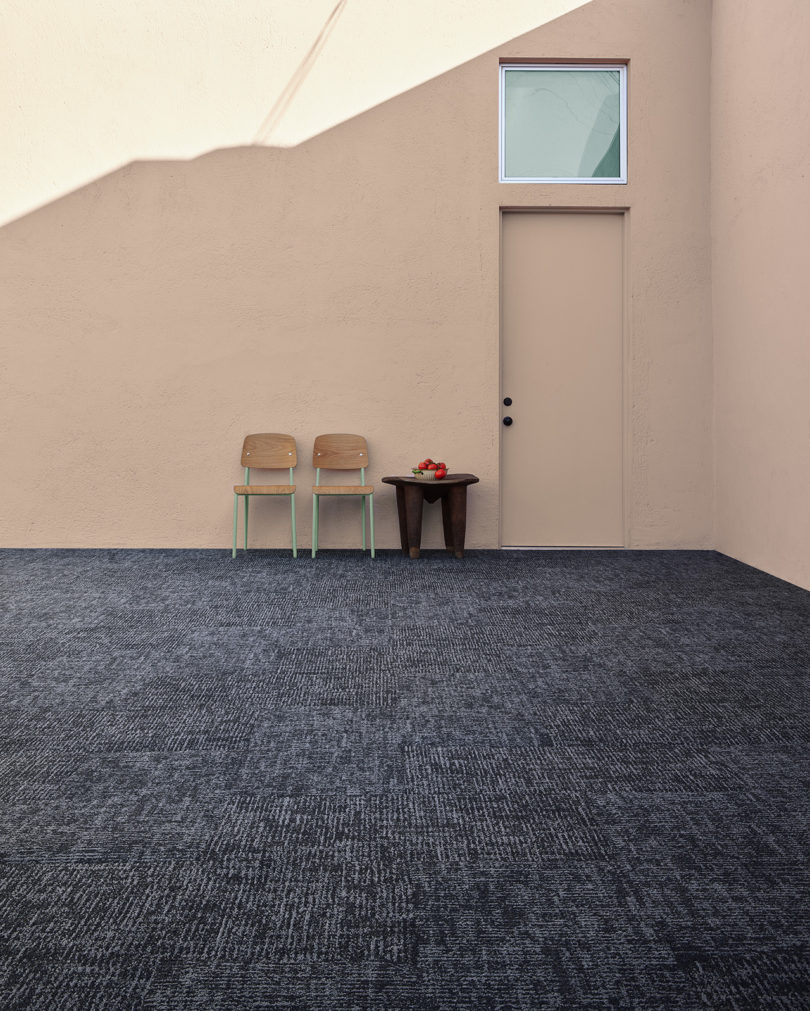 large space with dark grey/blue commercial carpeting, light pink walls, two chairs, and a side table