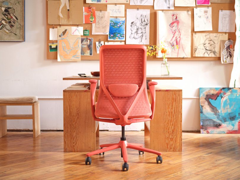 office with coral colored office chair, desk, and illustrations hanging on a cork board