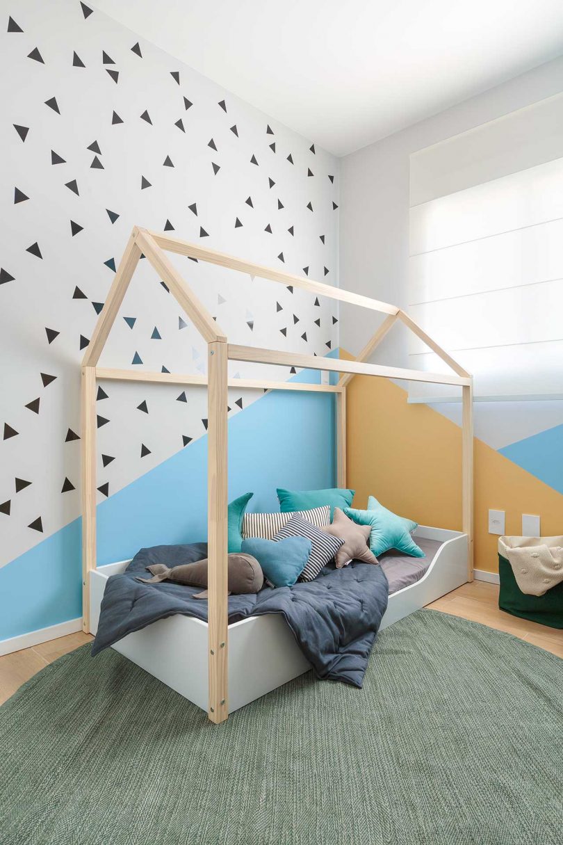 نمای زاویه‌دار اتاق کودک مدرن با دیوارهای گرافیکی آبی و هلویی و تخت‌های قاب‌دار