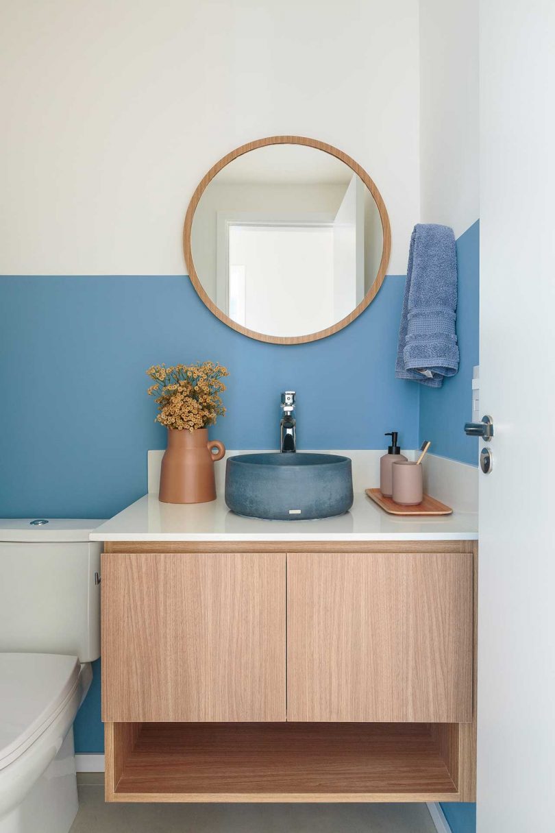 small modern bathroom with wood vanity and thick blue stripe on wall and round blue raised basin