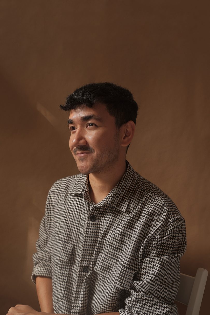 brown-skinned man with dark hair and mustache wearing a grey button down shirt