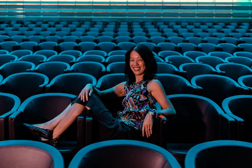 dark-haired woman sitting in an empty theater and smiling