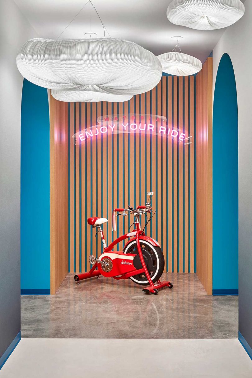 stationary bike in a workplace alcove with a neon sign reading Enjoy Your Ride hanging on the wall