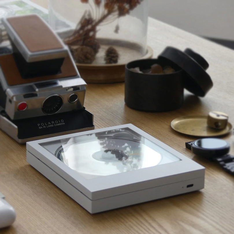 CP1 CD player on wood surface near instant film camera, black watch and other small tabletop items blurred in the background. 