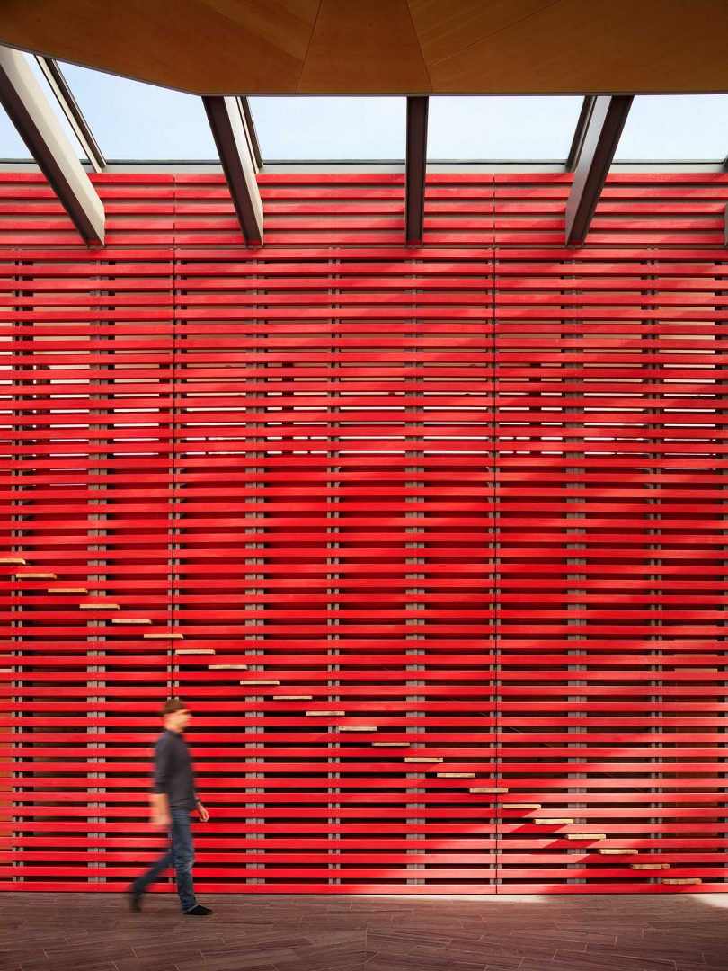 double height open red slatted wall with stairs behind it