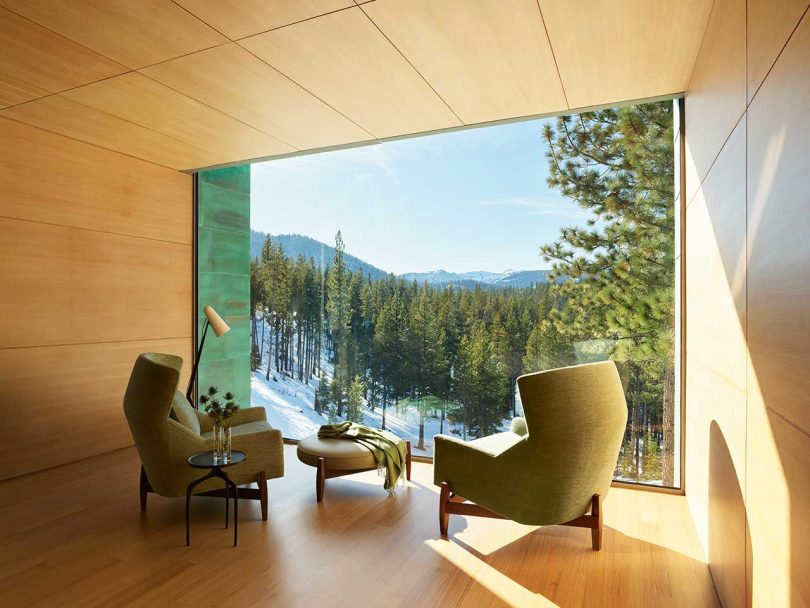 seating vignette with two green chairs in front of large window looking out to snowy landscape
