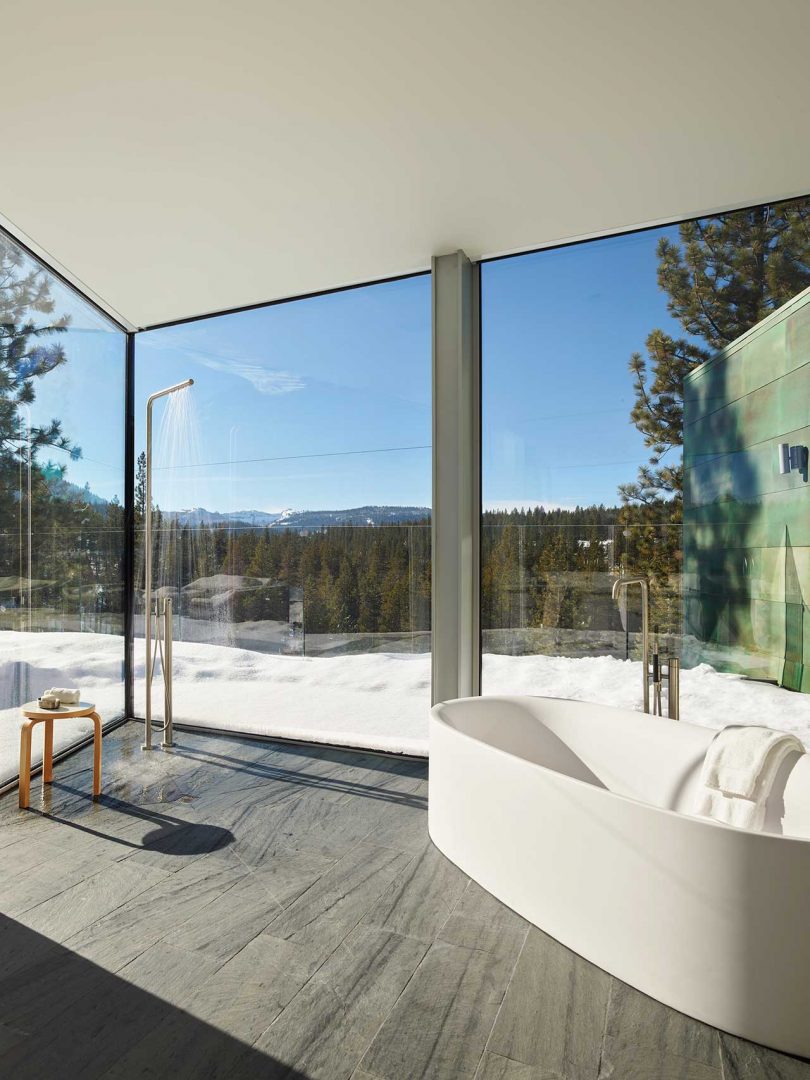 large modern bathroom with two glass walls looking out to snowy landscape