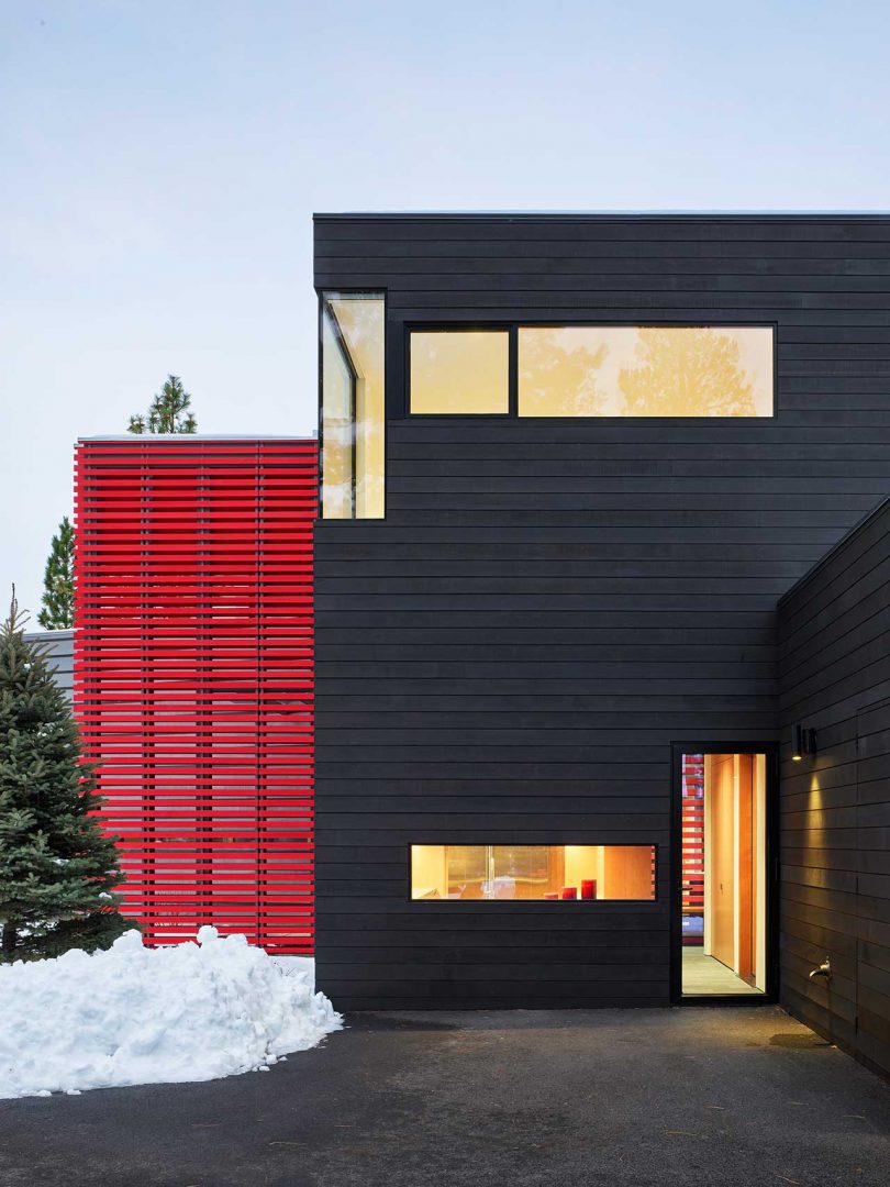 Snowy exterior shot of modern home with black slatted volume and red slatted volume