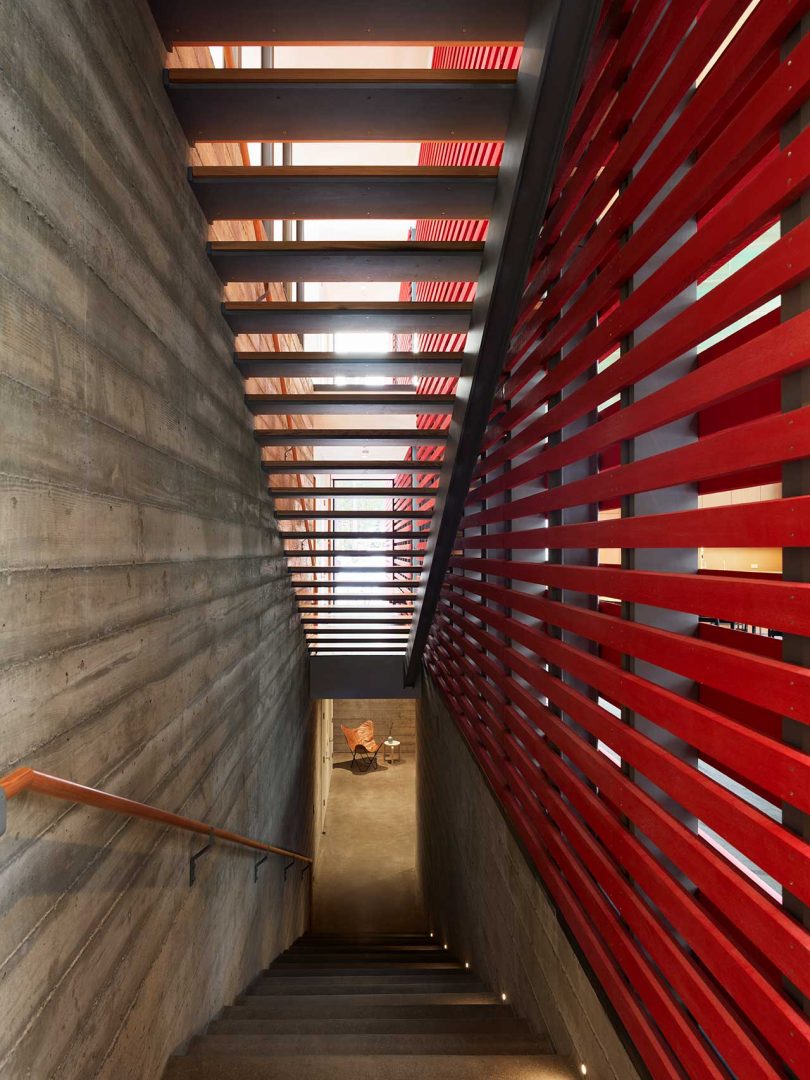 set of stairs leading down to basement with open stairs above and red slatted wall to side