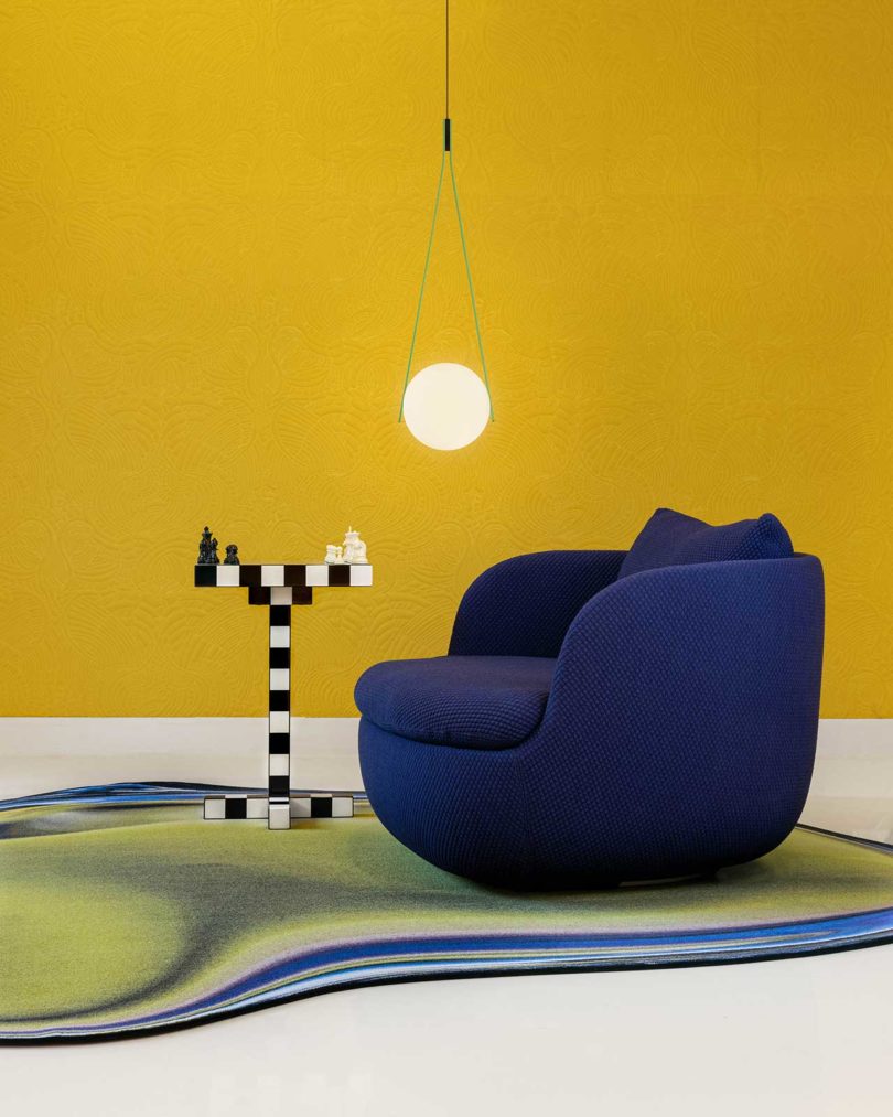 گوی روشن معلق با صندلی راحتی آبی تیره، میز کناری و فرش رنگارنگ کف در مقابل دیوار زرد رنگ