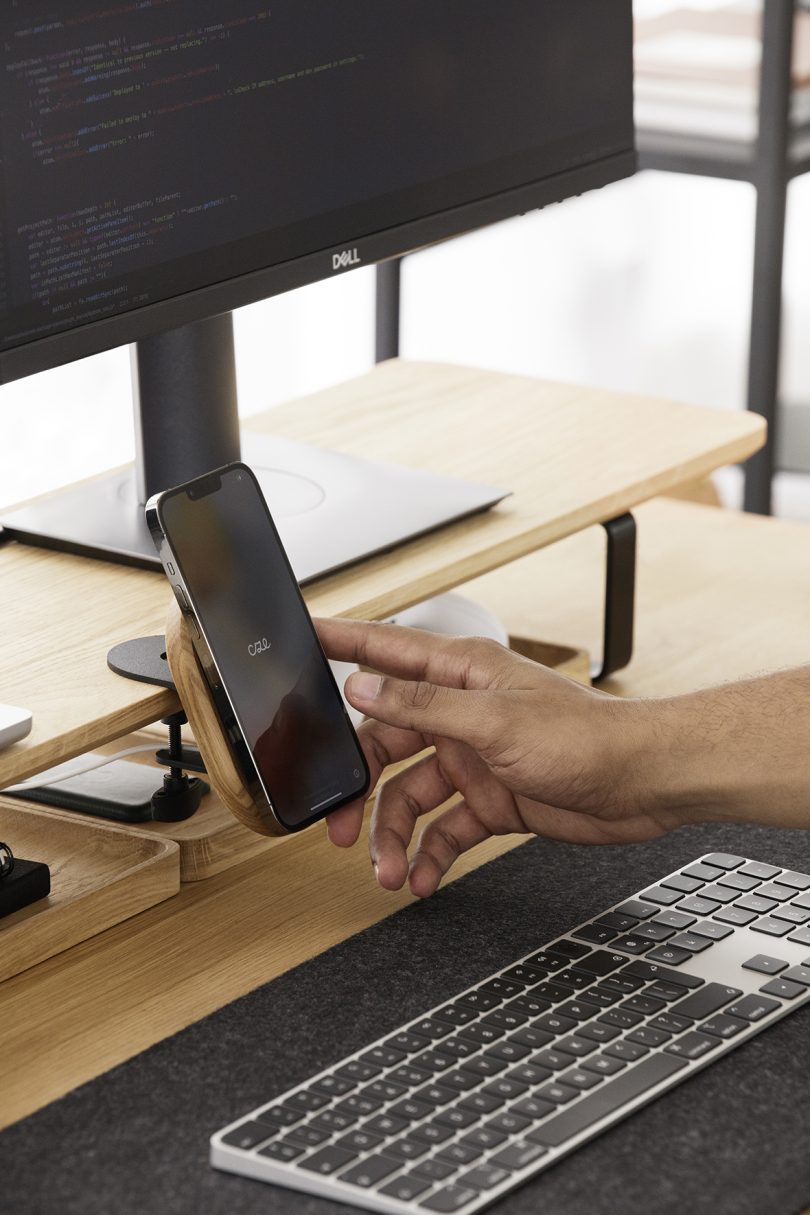 a hand interacting with an iPhone that's been mounted to a wooden desk shelf