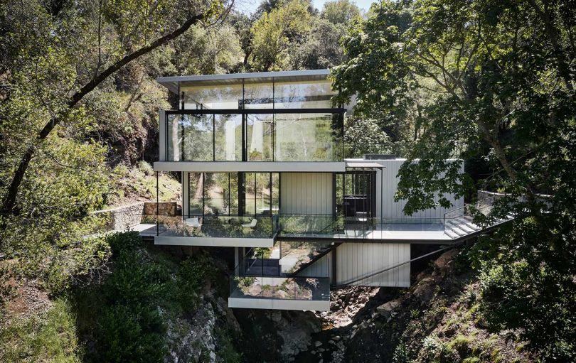 exterior view of multi story modern house built over river between two hills