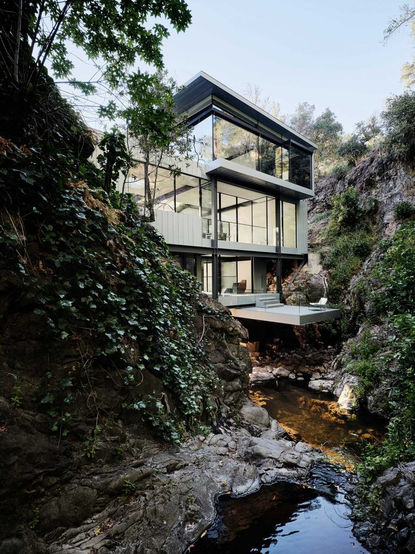 multi story modern house built over river between two hills