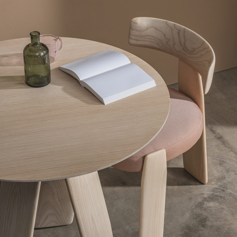light wood dining chair with light pink upholstery and three-legged light wood dining table