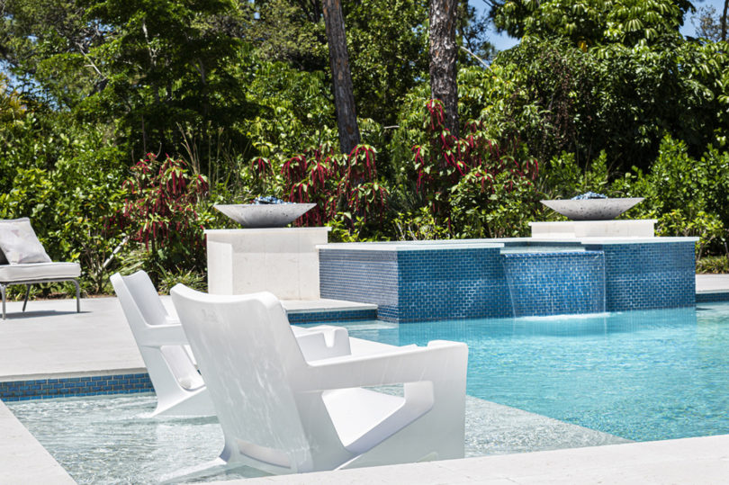 two white outdoor armchairs in the shallow end of a modern pool