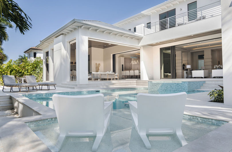 two white outdoor armchairs facing a pool and modern home