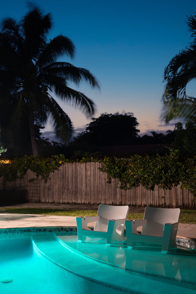 two white outdoor armchairs in the shallow end of a modern pool at night