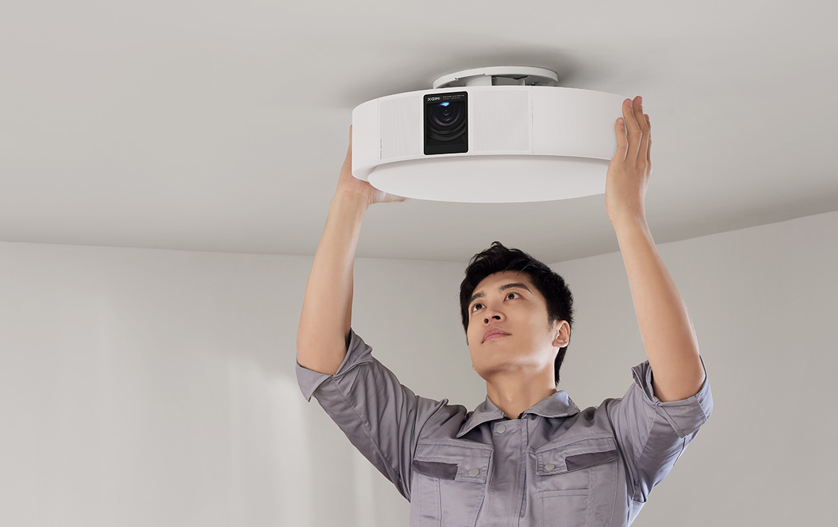 Asian man installing a circular movie projector onto the ceiling.